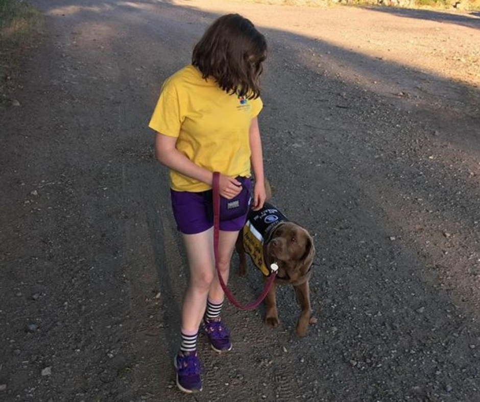 child in a yellow top walking their brown dog who is wearing their pawsitive squad jacket